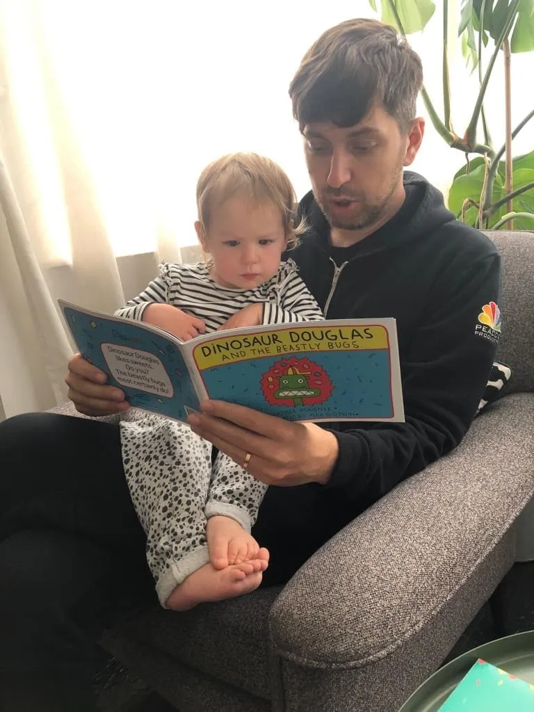 A father reading Dinosaur Douglas and the Beastly Bugs to a toddler sitting on his lap